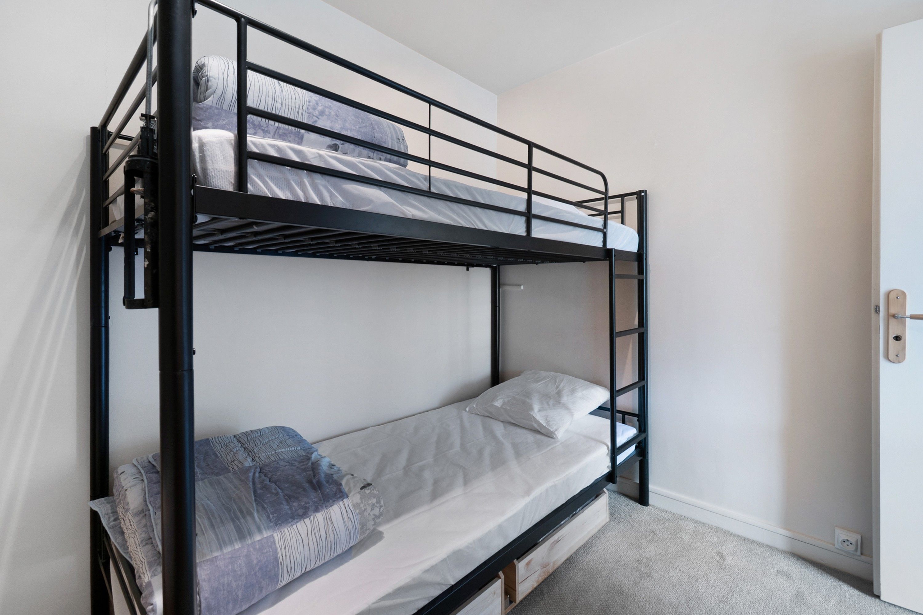 A bunk bed with a ladder, a single bed below, and a door to the right.