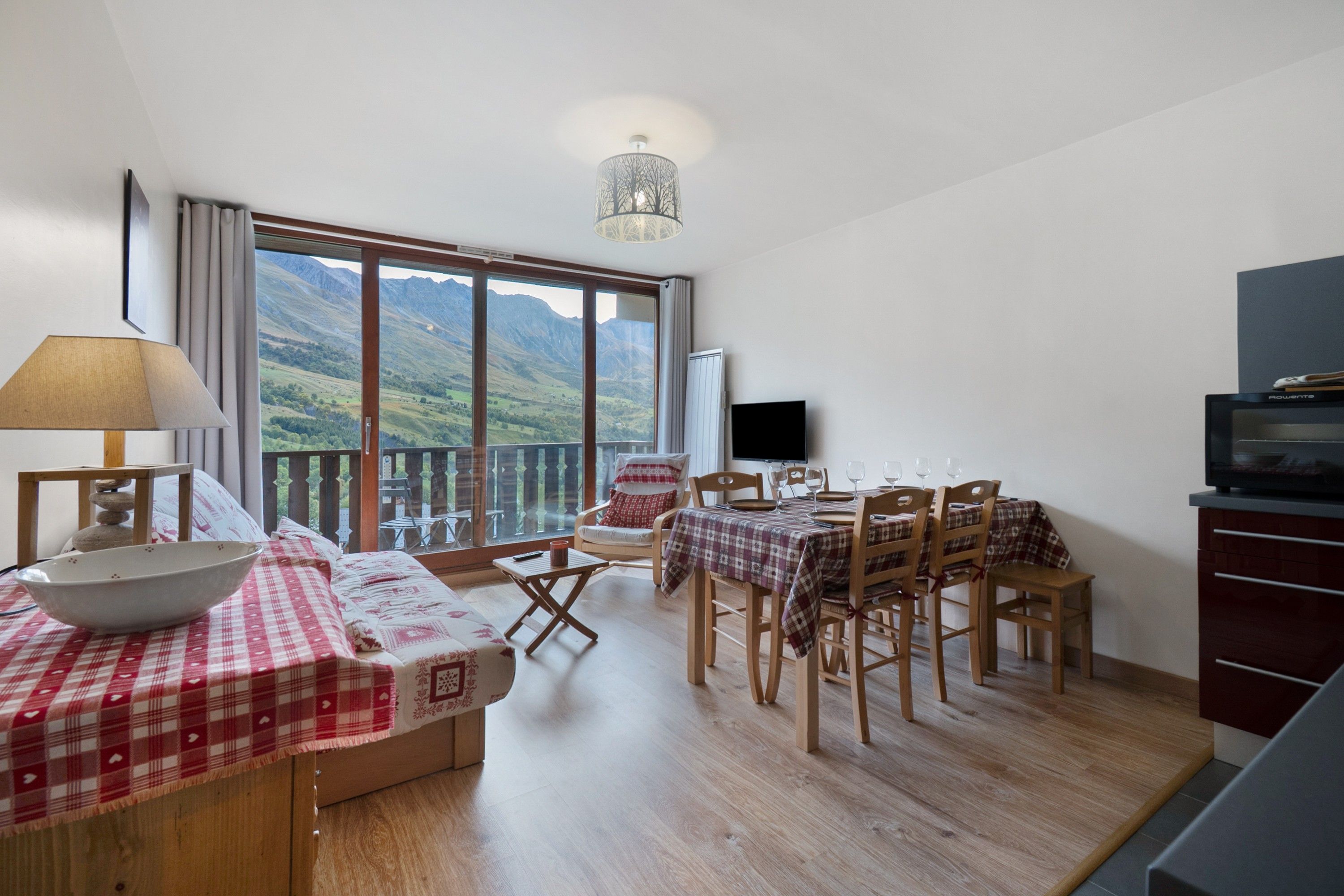 A room with a dining table set for four, a television, and a view of mountains.