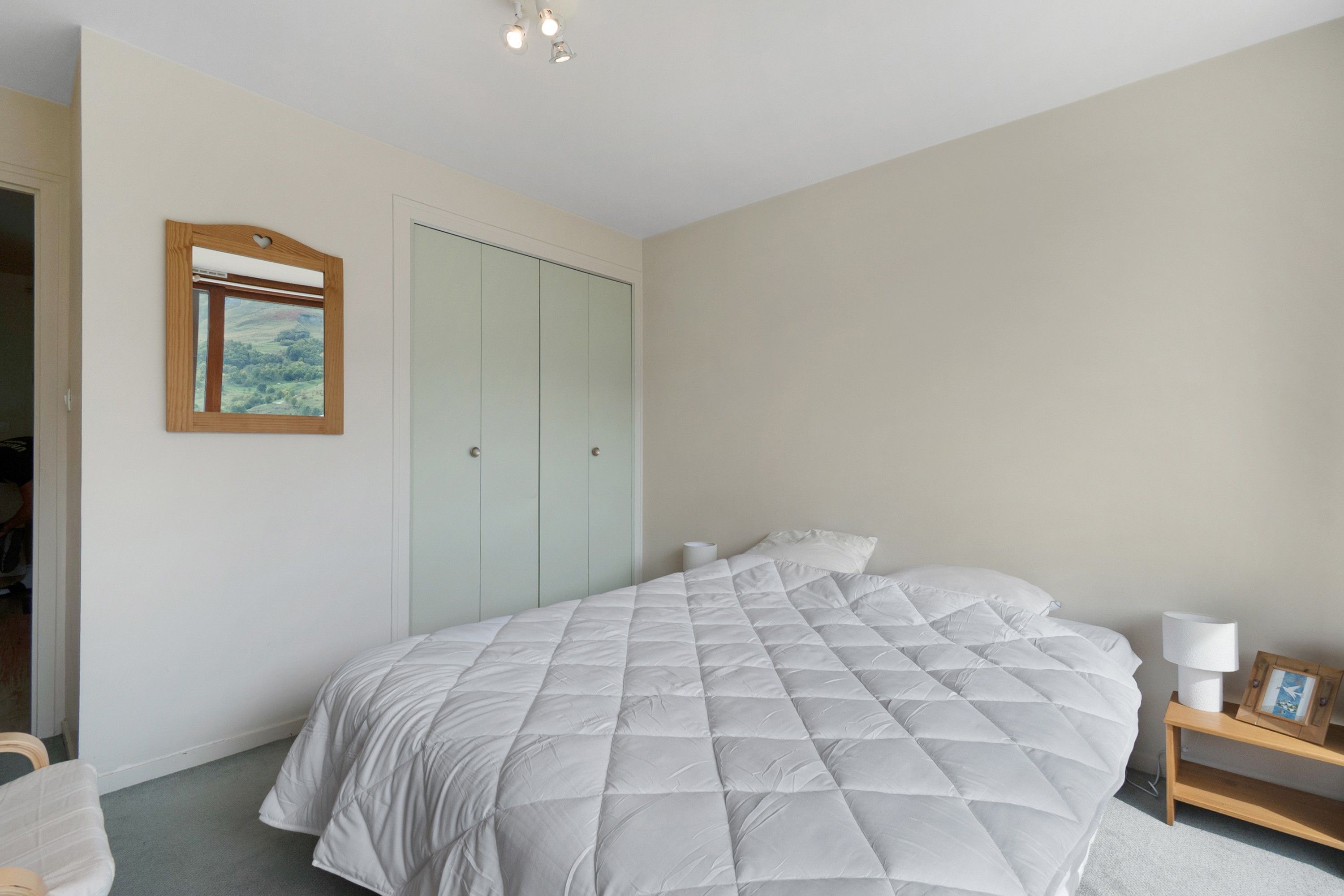Een slaapkamer met een groot bed, een kledingkast, een nachtkastje met lamp en een lijst met een afbeelding aan de muur.