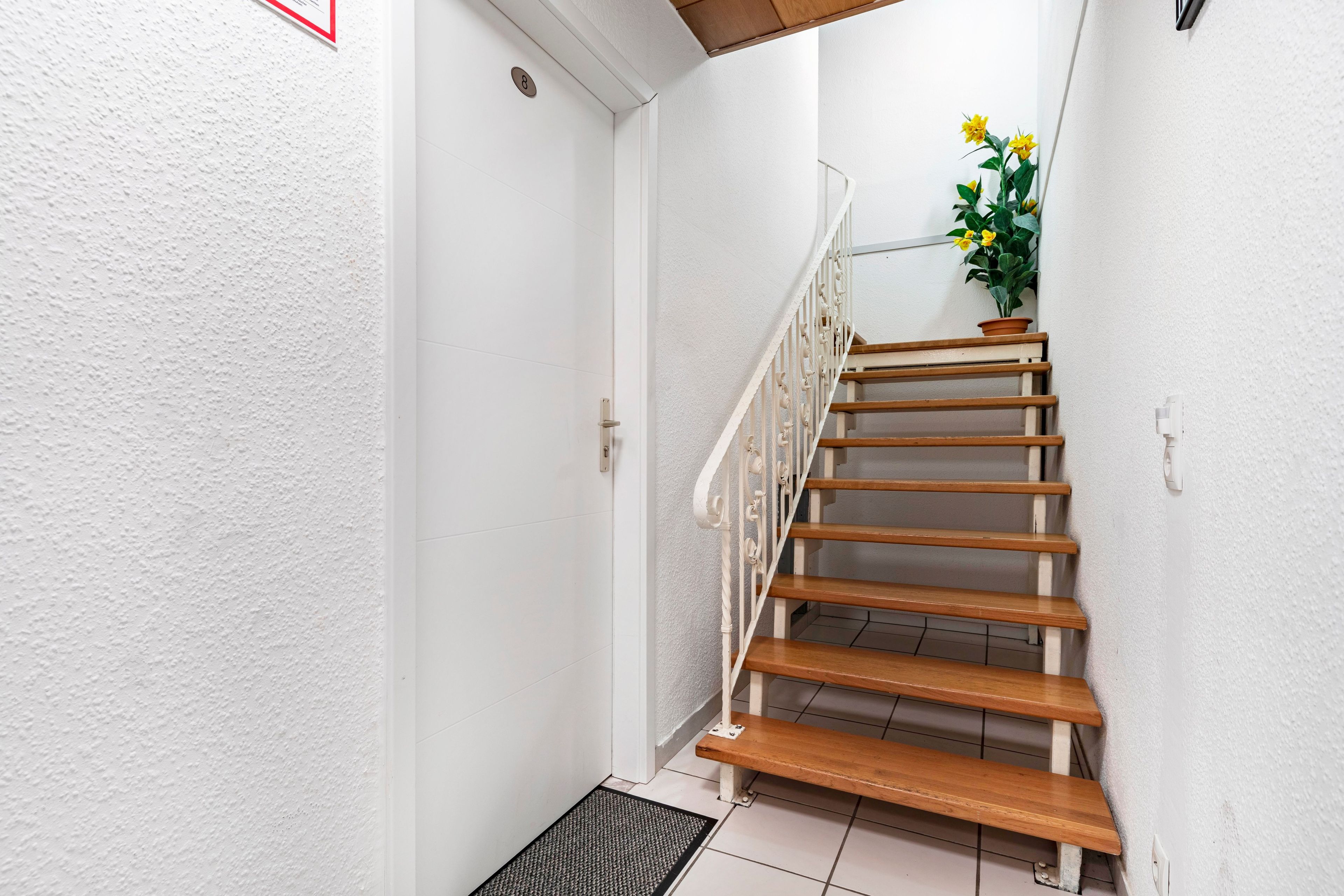 Eine Treppe mit Holzhinweisstufen und weißen Geländern, die zu einer Zwischenebene mit einem Blumentopf führt.