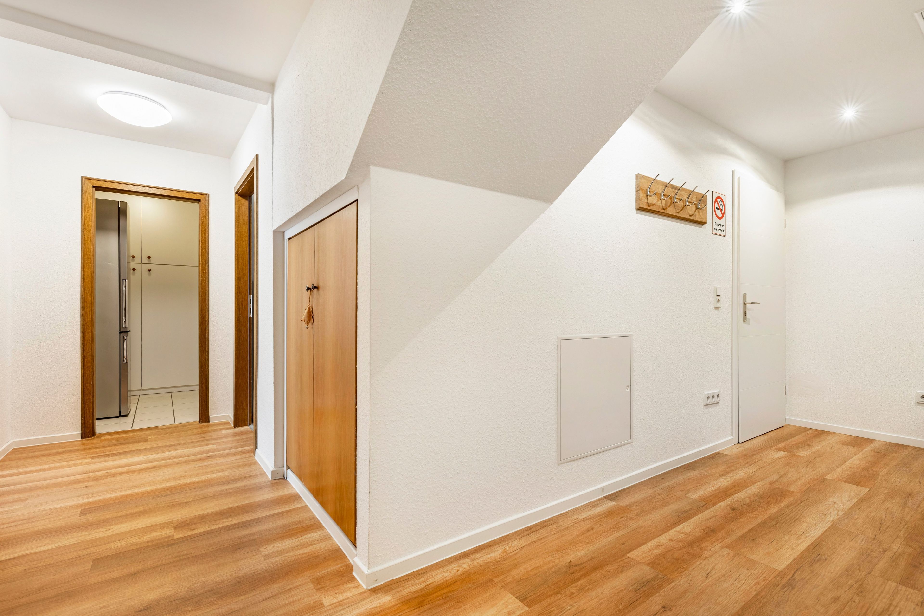 A hallway with wooden flooring, white walls, and a door with a wooden frame.
