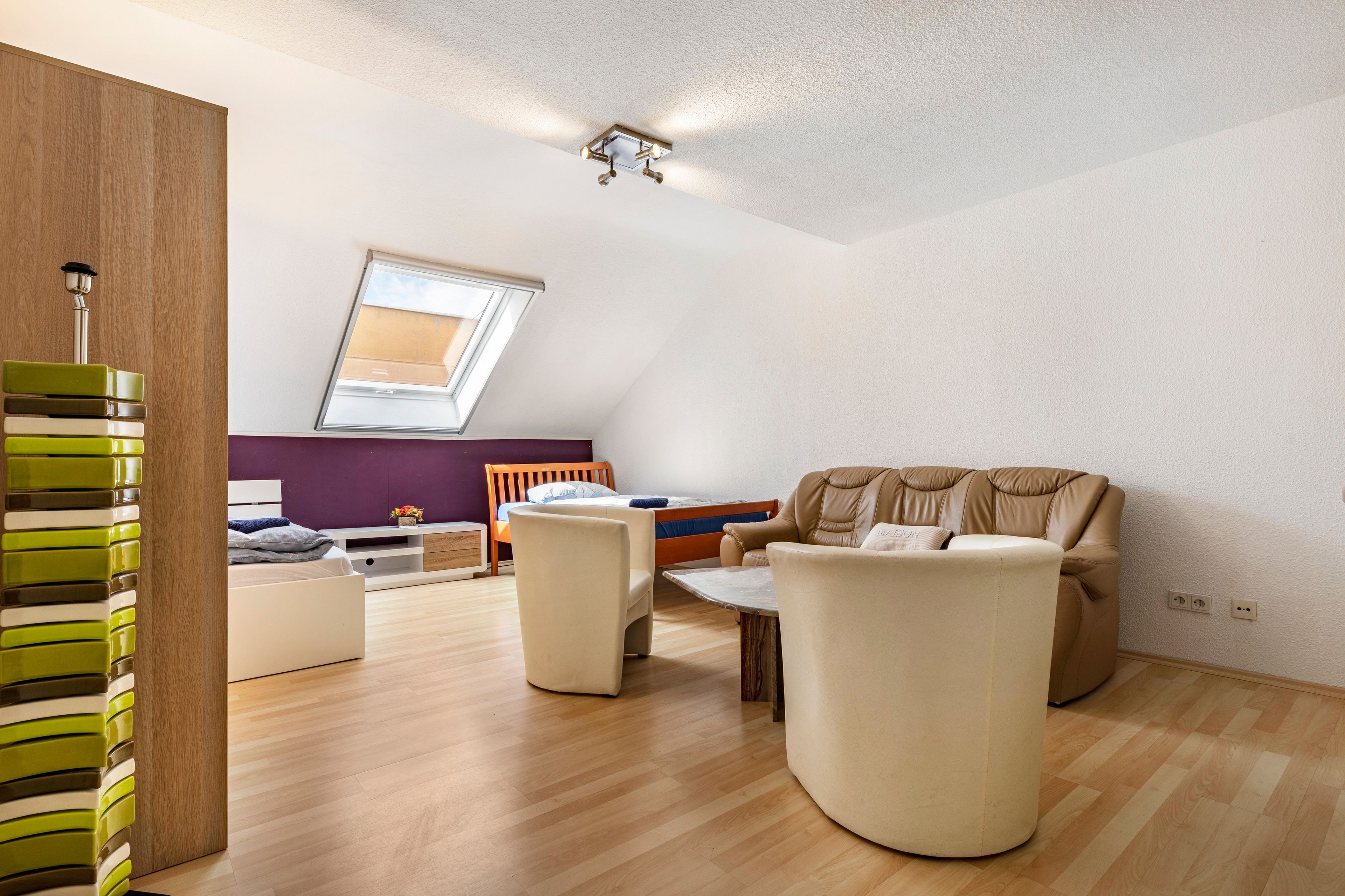 Ein modernes Schlafzimmer im Loft-Stil mit schrägen Wänden, einem Oberlicht, einem Bett, einer Couch und einem Couchtisch.