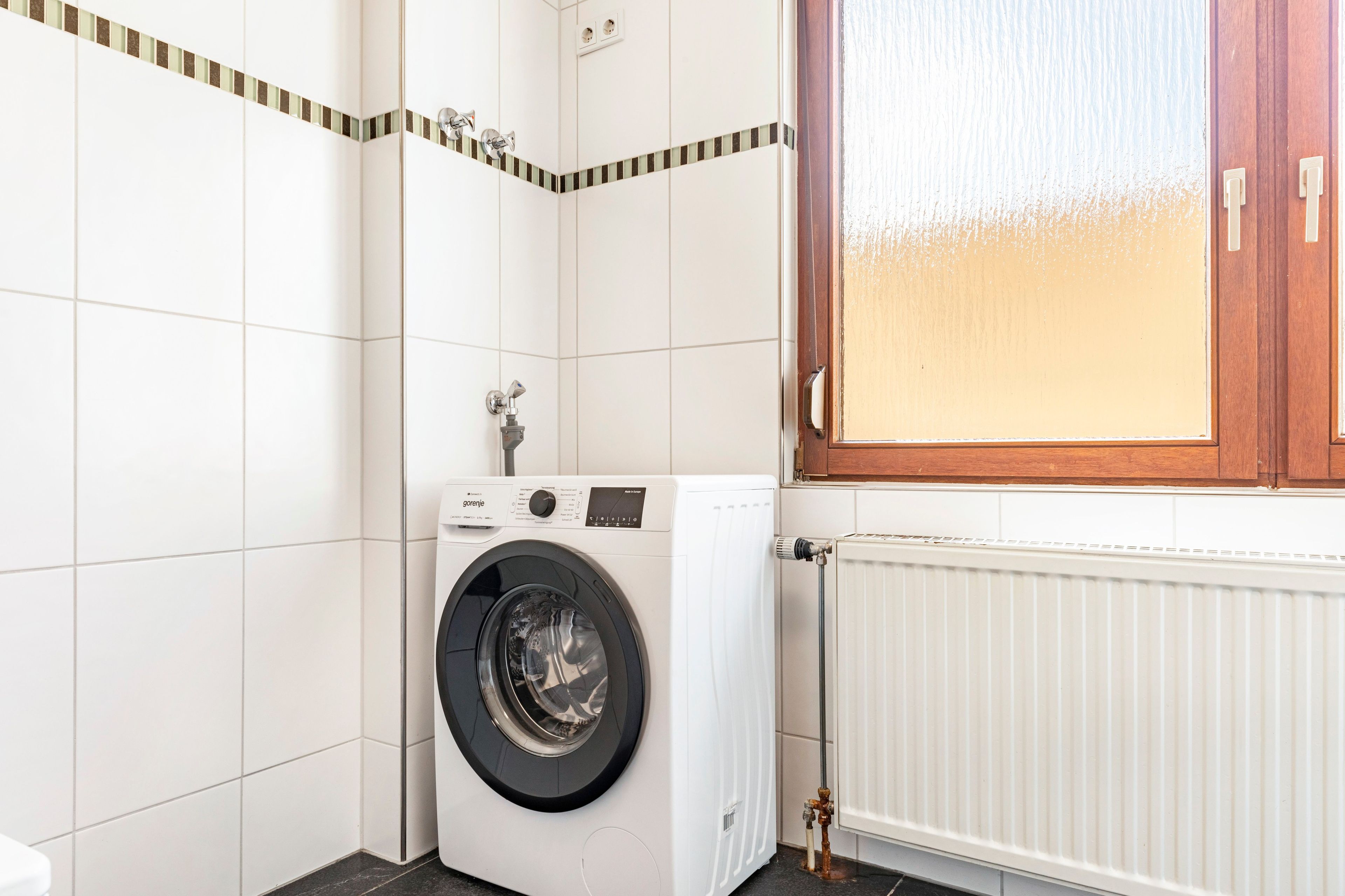 Ein kleiner Hauswirtschaftsraum mit einer Waschmaschine, einem Heizkörper und einer Holztür.
