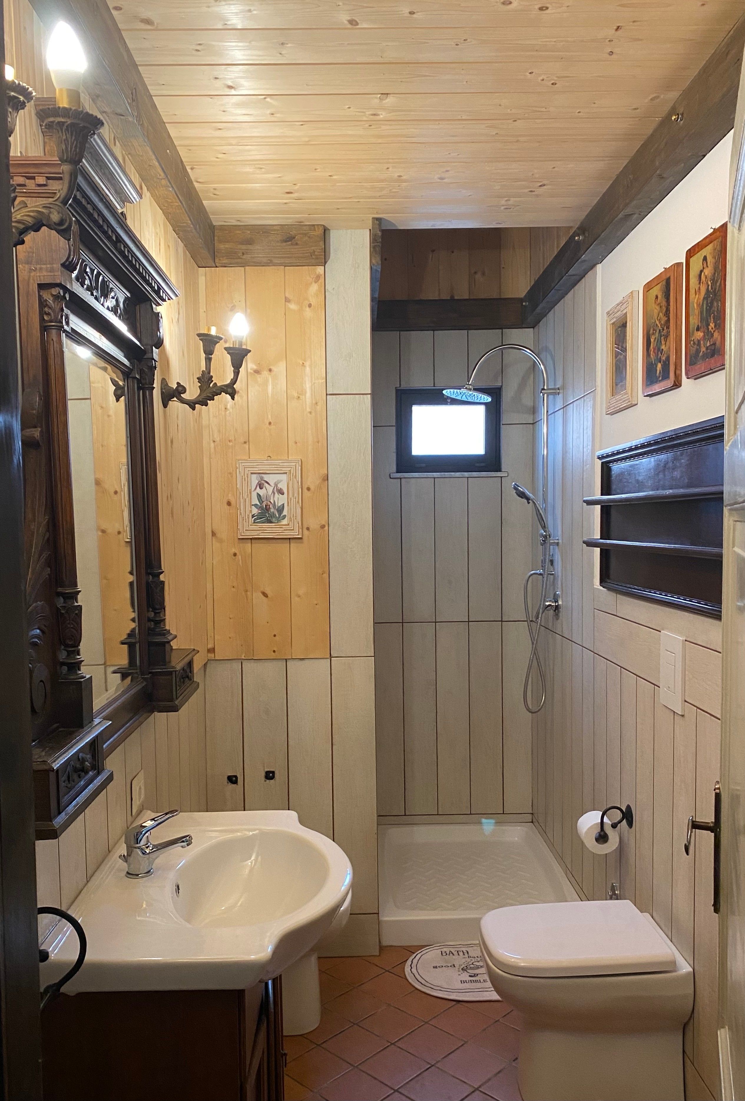 Un bagno con rivestimenti in legno, un lavandino, un water, una doccia e uno specchio con decorazioni elaborate.