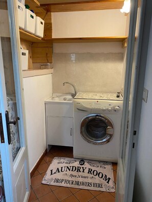 A laundry room with a washing machine, a dryer, and a sink. There is a sign on the floor indicating it's a self-service laundry room open 24 hours.