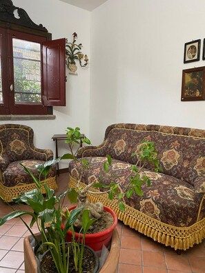 A living room with a patterned sofa, two armchairs, a wooden cabinet with a glass door, and a potted plant. - Viale del Re 33: Your Vintage Retreat Steps from the Sea in Catona (RC) (Reggio Calabria)
