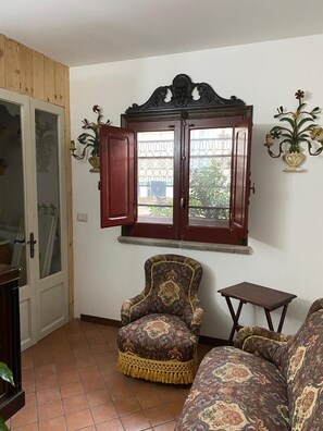 A living room with a patterned armchair, a sofa, a small table, and a decorative cabinet with open doors.