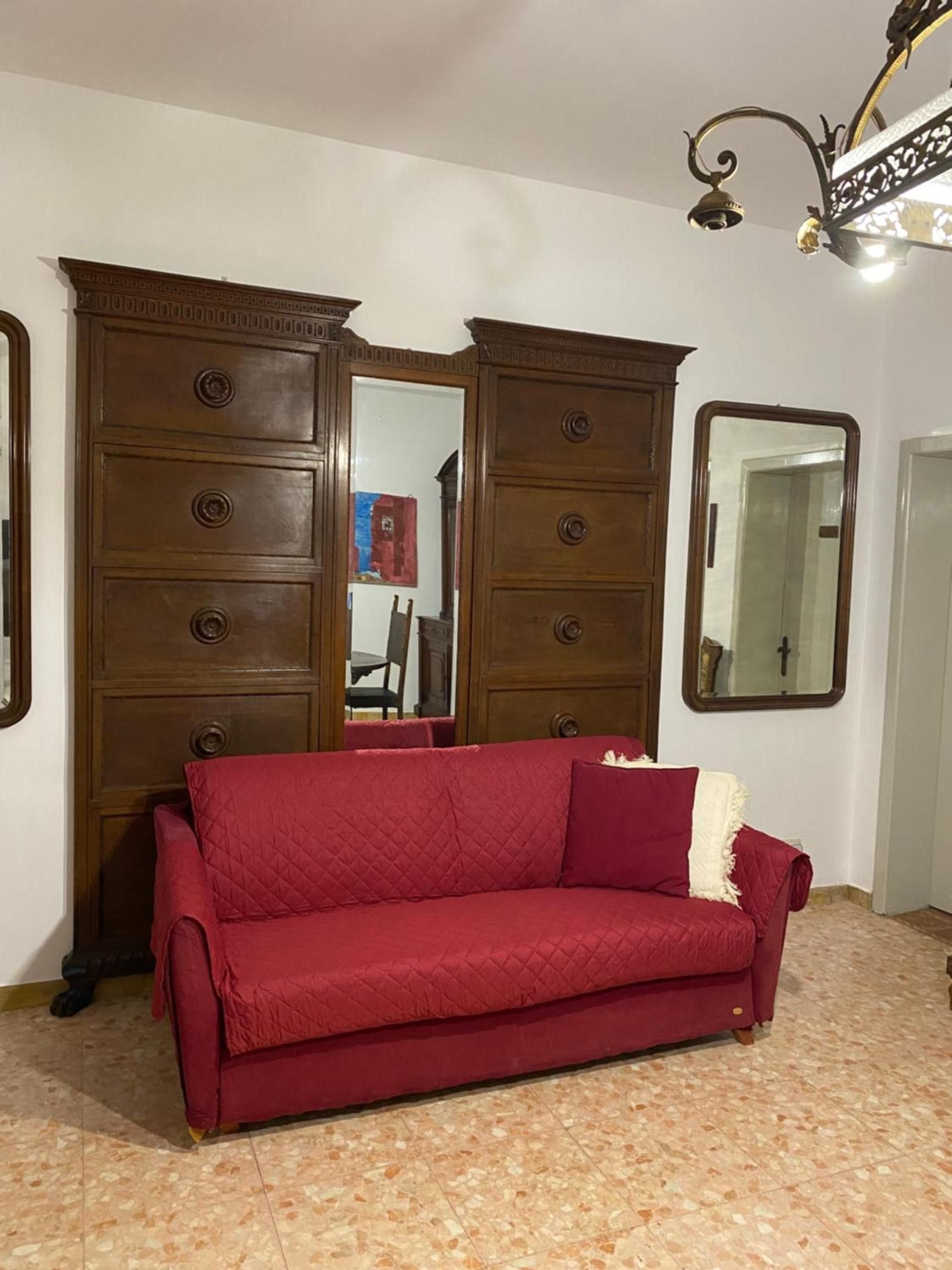 Una stanza con un divano rosso, un'ampia armadiatura in legno, uno specchio e un lampadario.