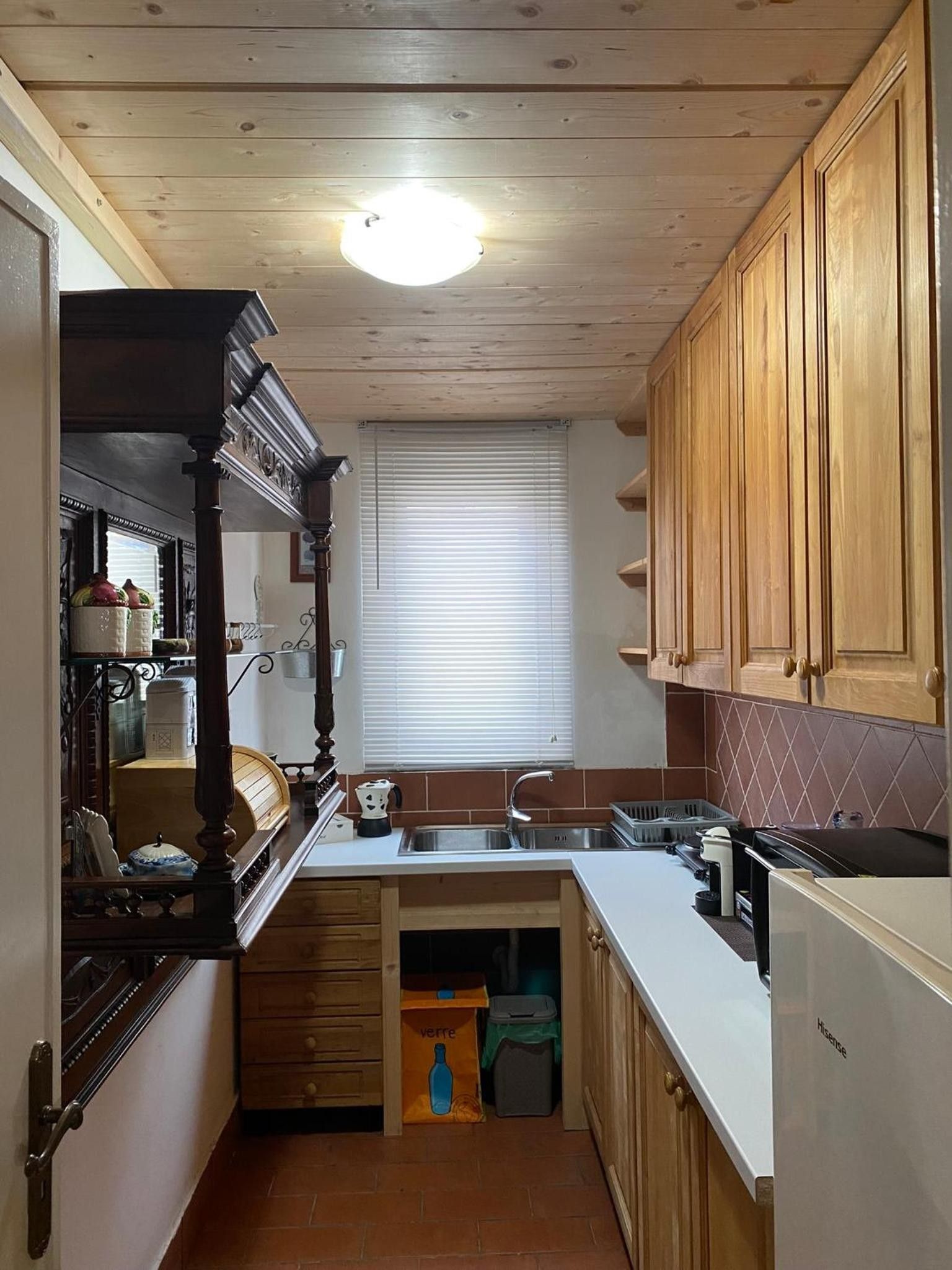 Una cucina stretta con mobili in legno, forno integrato e una finestra con persiane.