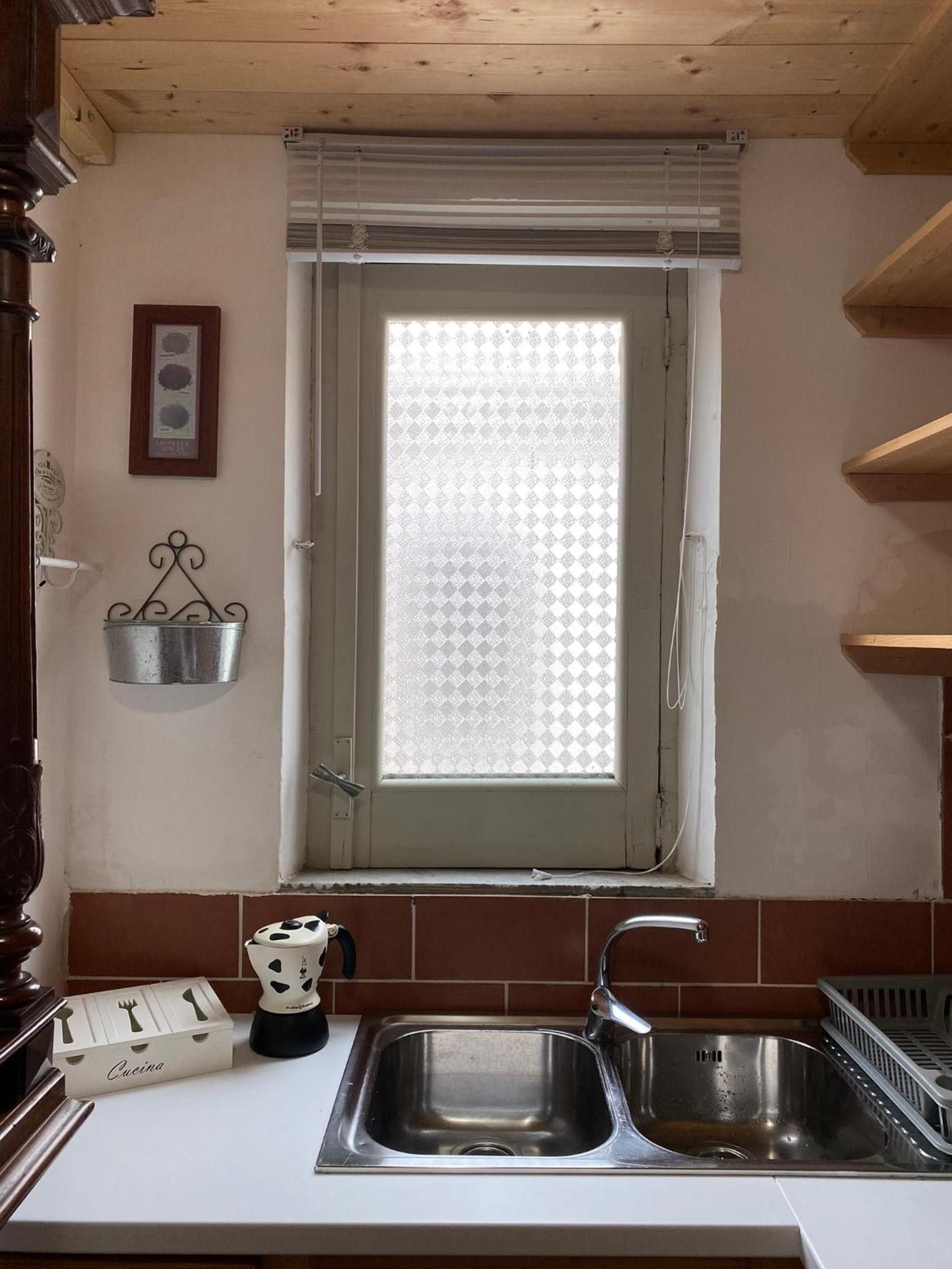 Eine Küche mit Fenster, einem Spülbecken, einem Metallkübel und einer weißen Box mit dem Aufdruck 'Cucina'.