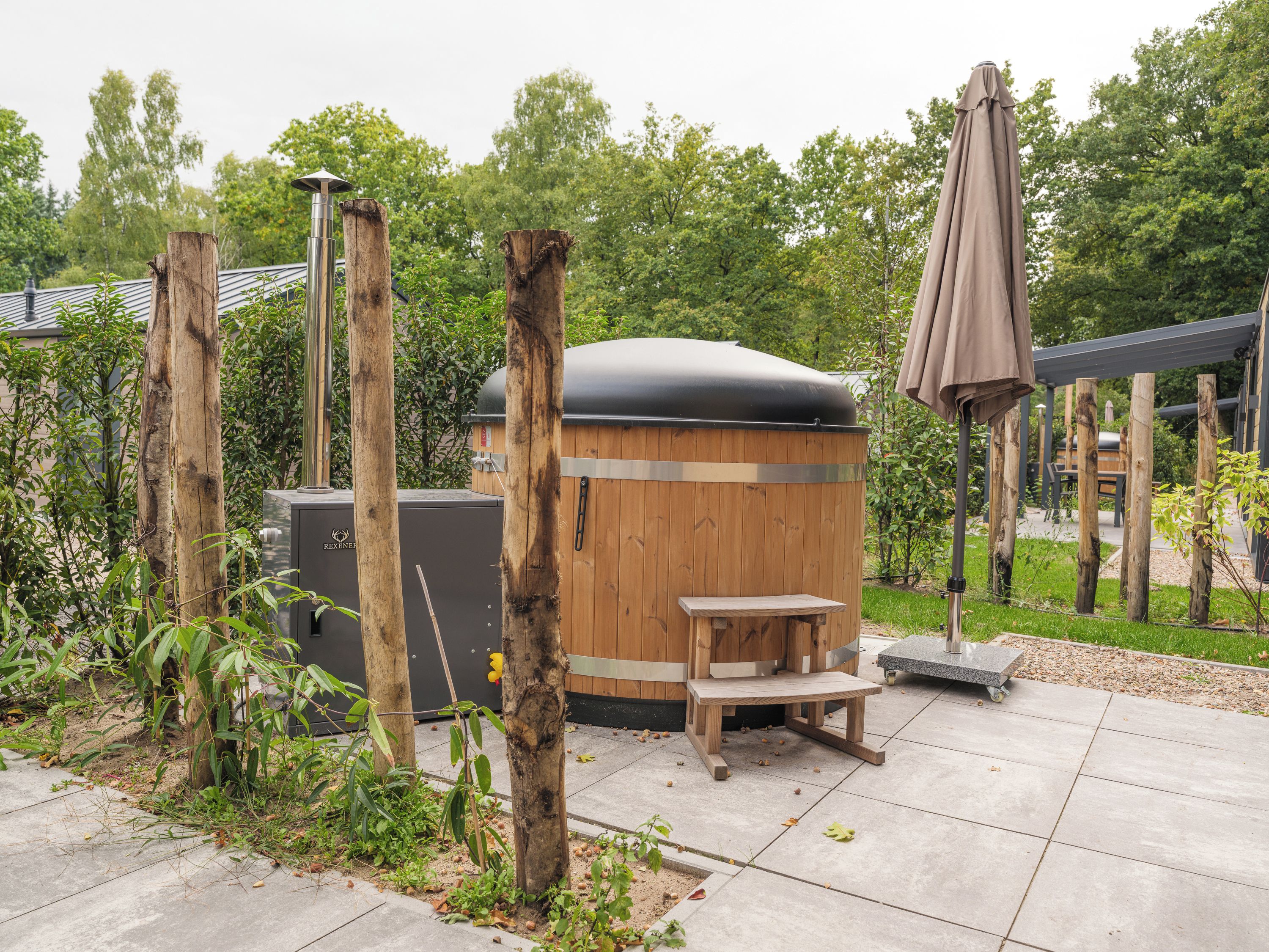 Een houten jacuzzi met een bankje en een tafeltje, omgeven door bomen en een terras.