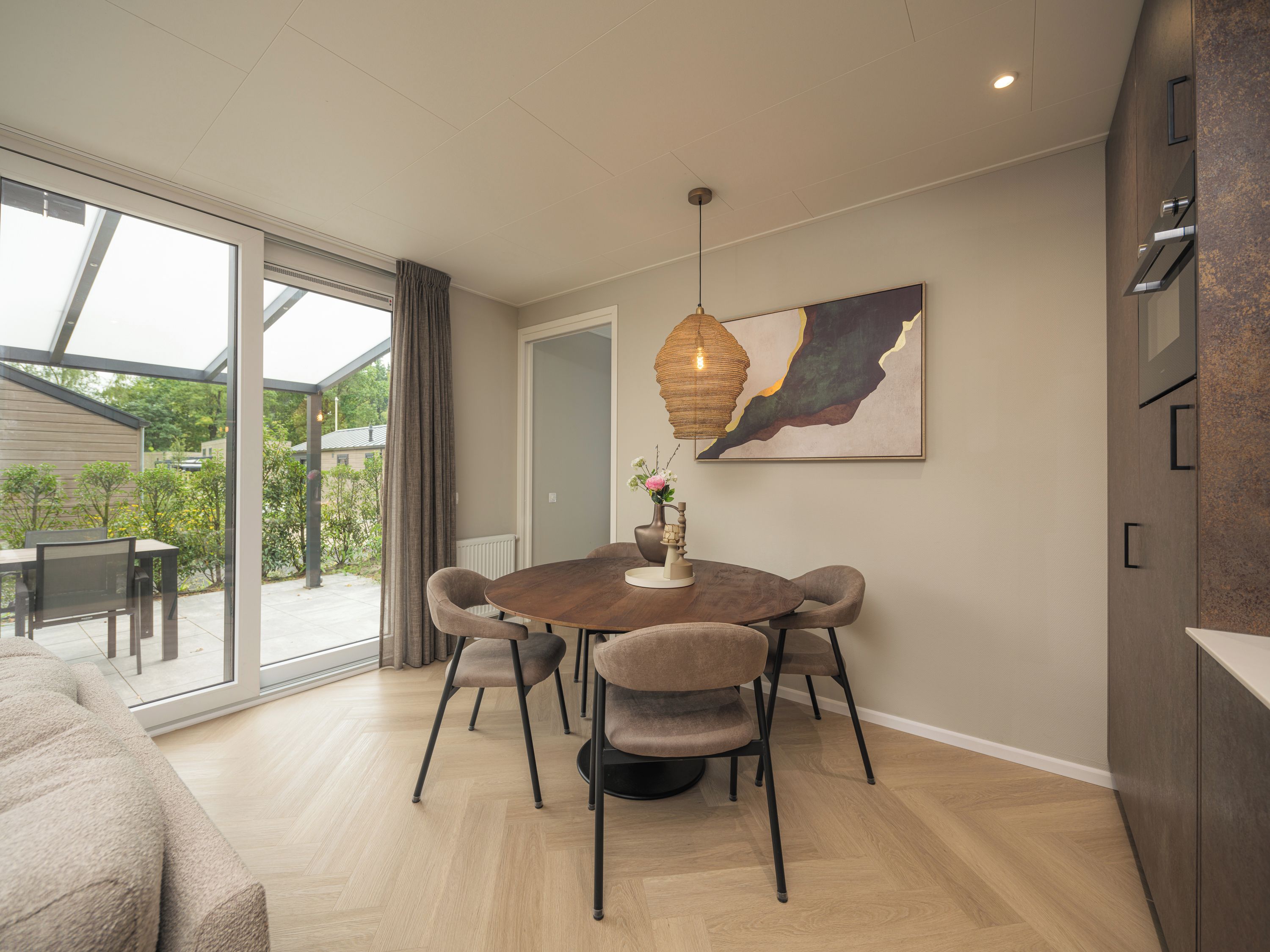 Een moderne eethoek met een ronde tafel, zes stoelen en een hanglamp.