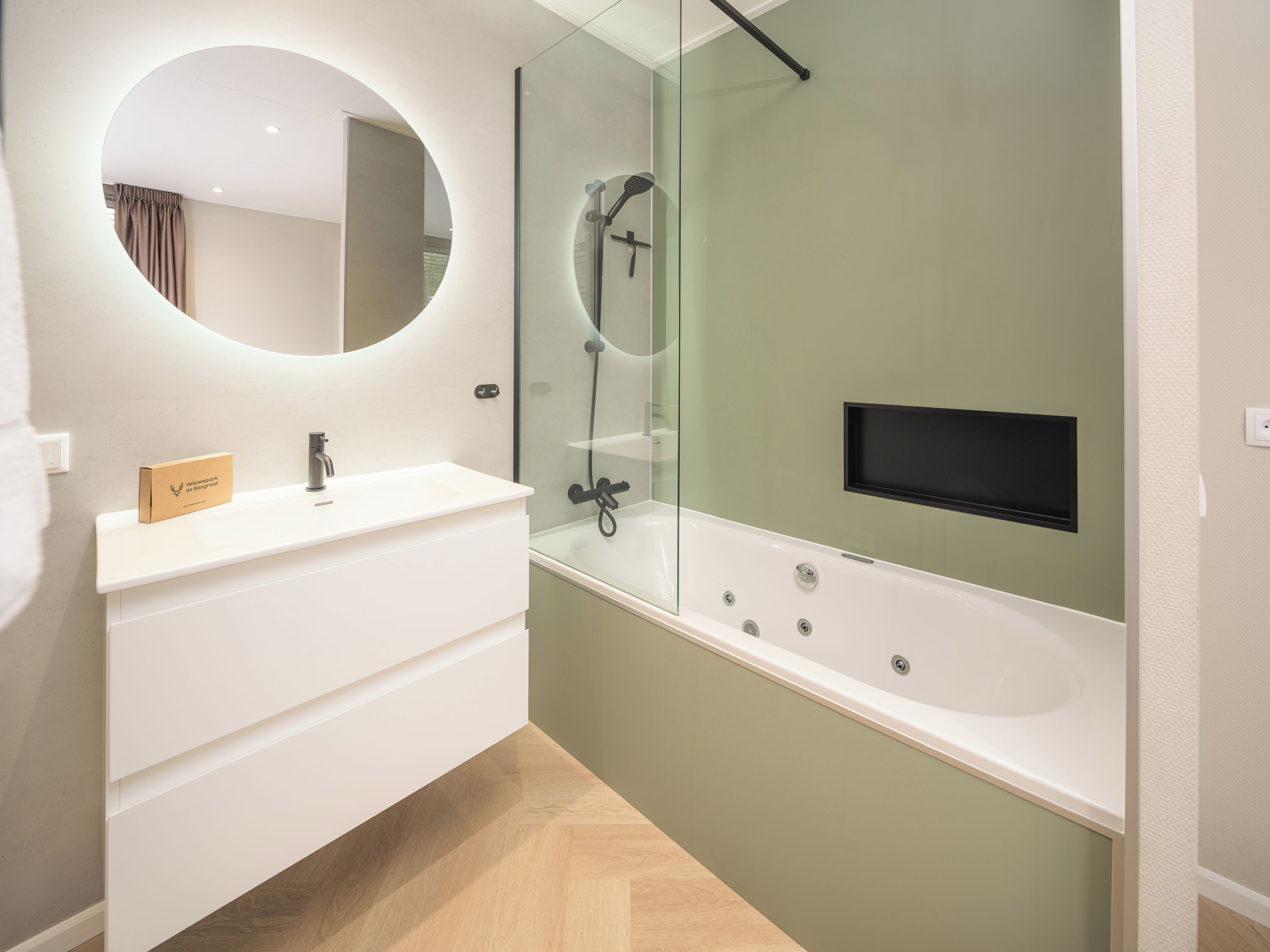 Een moderne badkamer met een ronde spiegel, een wit wastafelmeubel, een douche met glazen wanden en een ingebouwde televisie.