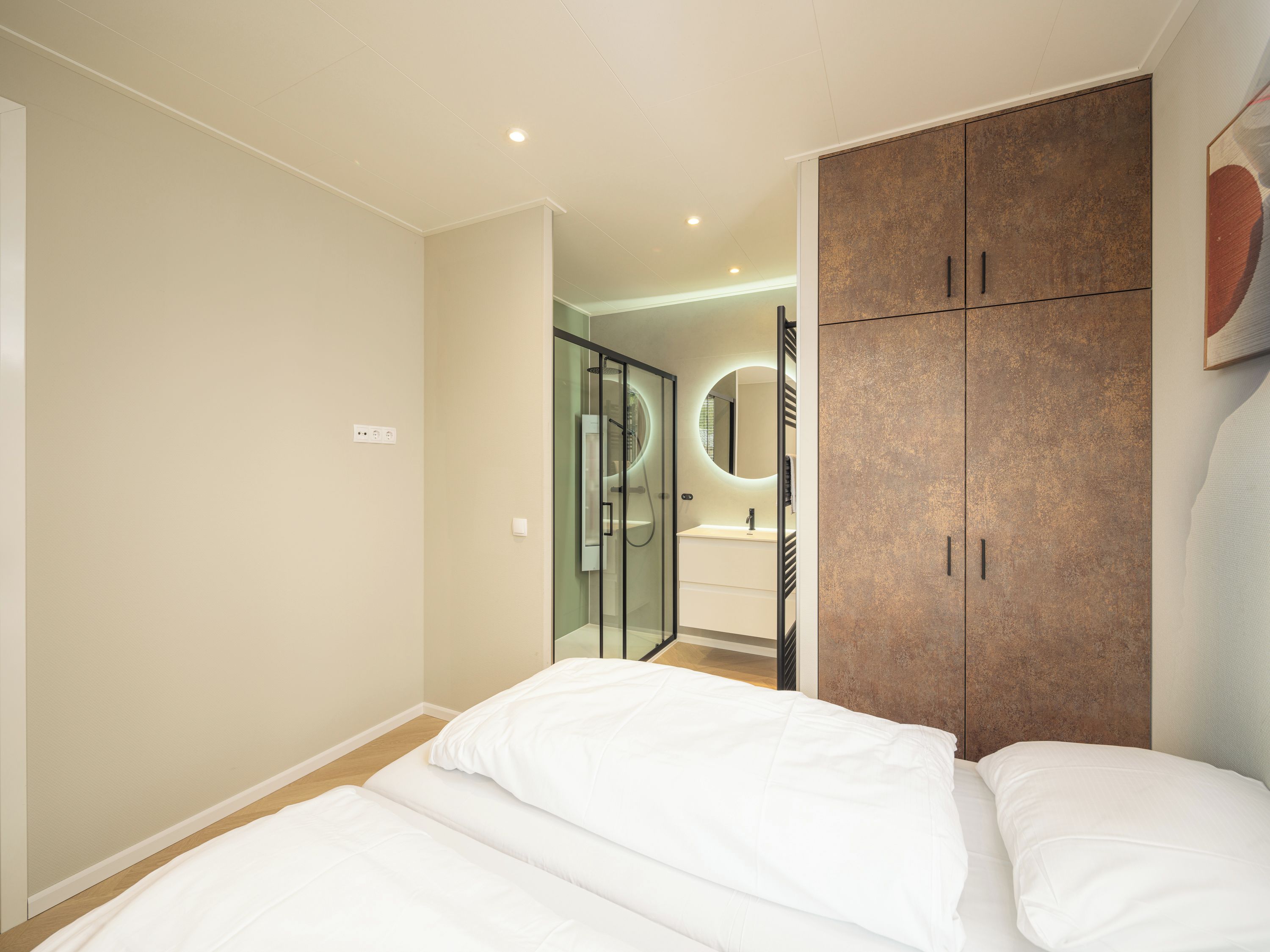 Camera da letto con un letto, un armadio e un bagno visibile attraverso una porta in vetro.