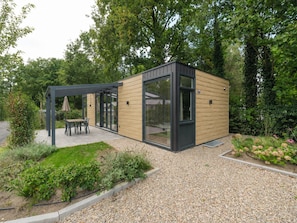 A modern outdoor patio with a table and chairs, surrounded by a garden with various plants and flowers. - Rosendael Comfort | 4 personen: Stylish holiday home on the Veluwe for 4 guests, with air conditioning, two en-suite bathrooms featuring a whirlpool bath and sunshower, a partly covered terrace and a modern open kitchen. Your luxurious base in the he (Lieren)
