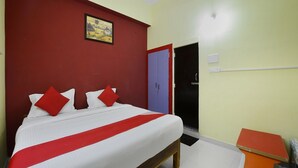 A hotel room with a bed, a red wall, a door, and a small orange table. - Hotel O Vellore Formerly SP Highway Inn (Vellore)