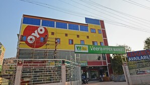 A multi-story building with a large yellow and red sign for 'Oyo' and a green sign for 'Veera Hyper Market.' - Hotel O Vellore Formerly SP Highway Inn (Vellore)