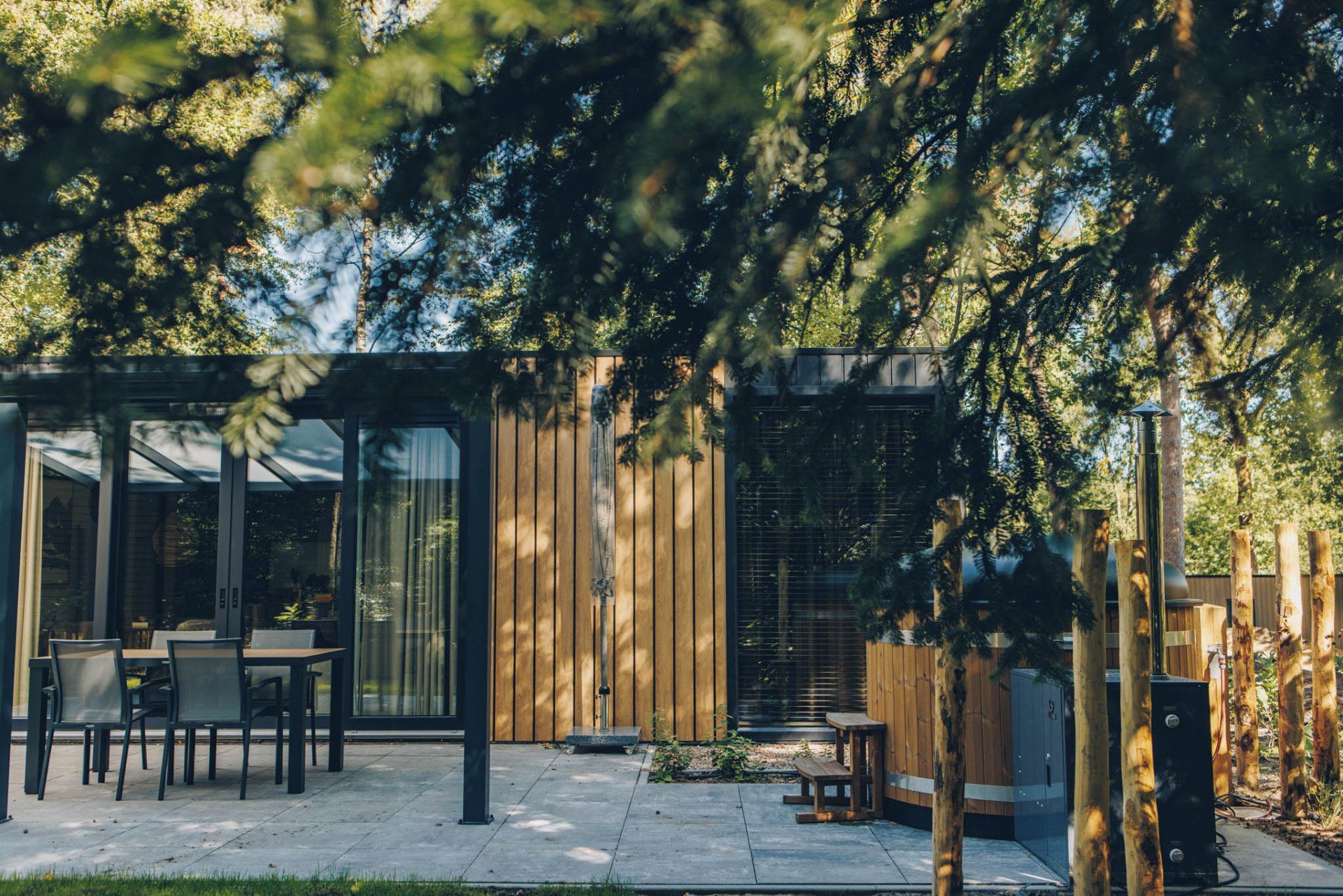 A modern outdoor patio with a glass enclosure, wooden deck, and seating area.