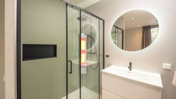 Een moderne badkamer met een douchecabine van glas, een wit wastafelmeubel en een ronde spiegel.