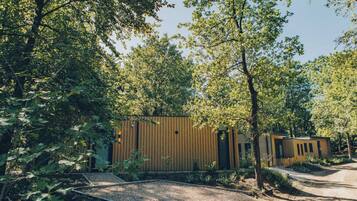 A modern building with a wooden facade, surrounded by dense foliage and a gravel path.