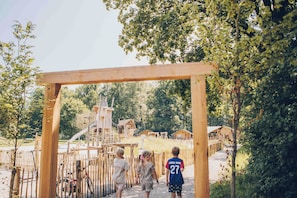 Ein hölzerner Bogen führt zu einem Spielplatz mit Rutsche und Klettergerüsten.
