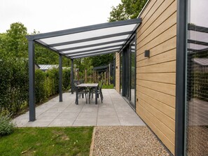 Ein überdachter Patio-Bereich mit Tisch und Stühlen, angrenzend an ein Gebäude mit Holzverkleidung.