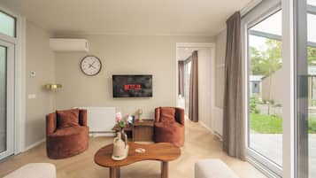 A modern living room with a large window, two sofas, a coffee table, a clock, and a TV displaying 'NETFLIX'.