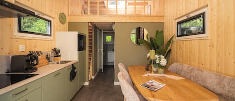 A compact kitchen with a dining area, wooden walls, and a view through a window.
