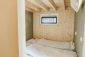 A room with a wooden ceiling, a window with blinds, and a bed with white bedding. - Wake up among the alpacas and sleep under the stars! From the Alpaca Retreat Lodge, you look out over grazing alpacas and enjoy the peace and nature of the Veluwe. In the open sleeping loft, the skylight creates a special experience: from bed, you lo (Lieren)