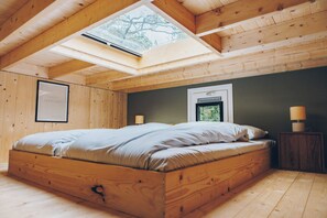 Ein Schlafzimmer mit einem hölzernen Bett, einem Oberlicht, einem Nachttisch mit Lampe und einem gerahmten Bild an der Wand.