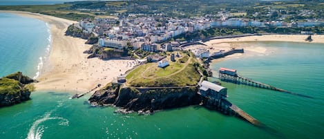 An aerial view of a coastal town with a beach, a fortified structure, and a pier.