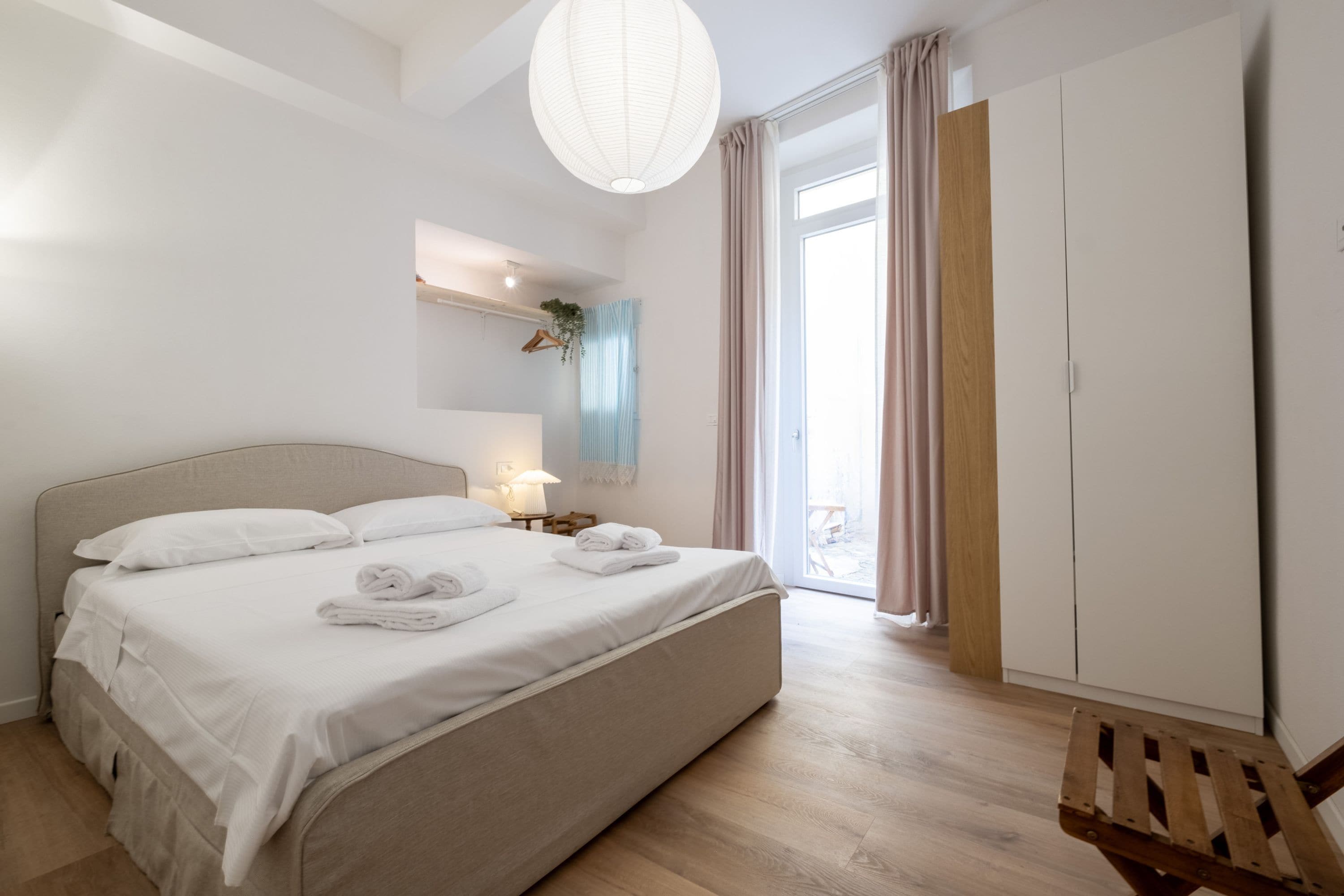 Un dormitorio moderno con una cama grande, lámparas de noche, una planta colgante y vistas al exterior a través de una puerta corredera.