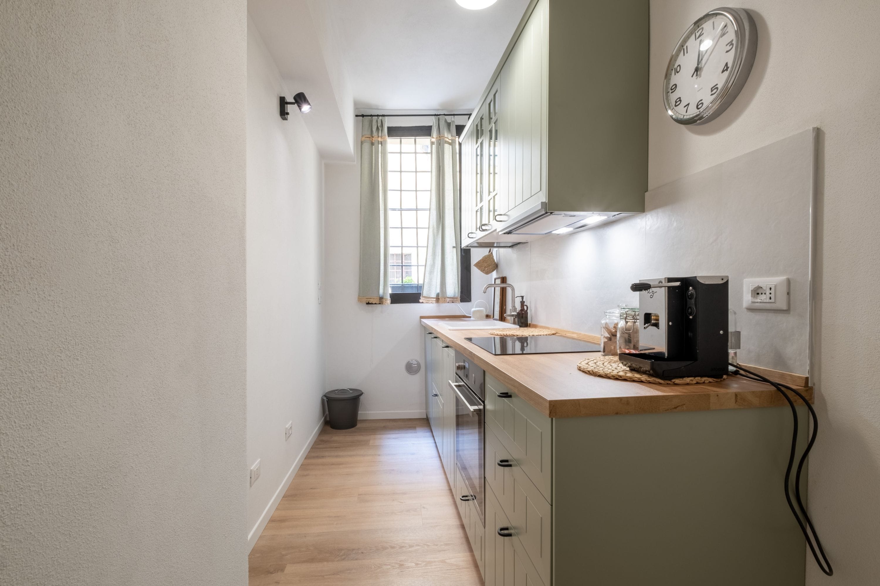 Una cocina estrecha con encimera de madera, una cafetera y un reloj en la pared.
