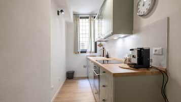 Una cucina angusta con un piano di lavoro in legno, una macchina da caffè e una sveglia appesa al muro.