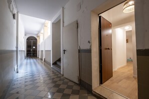Un corridoio con pavimento a scacchi che conduce a una porta in legno.