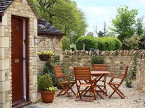 A stone building with a red door, a small outdoor seating area with a table and chairs, and potted plants. - Peewit Barn (Moreton-in-Marsh)