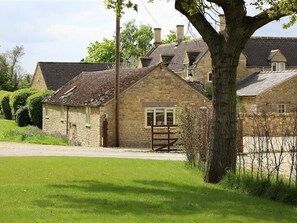 A stone house with a traditional design, a large tree in the foreground, and a clear sky. - Peewit Barn (Moreton-in-Marsh)