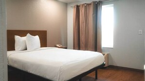Una habitación de hotel con una cama individual, teléfono en la mesita de noche y una ventana con cortinas.