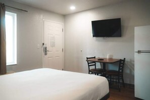 A hotel room with a bed, a desk with a chair, a television on the wall, and a door.