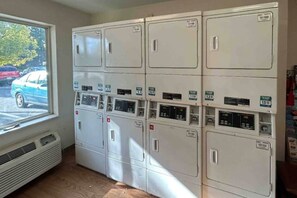 A laundry room with multiple washing machines and dryers, a window with a view of parked cars, and a vent on the wall. - 1 Queen Bed|Mobility|Nsmk|Kitchen (Rancho Cordova)