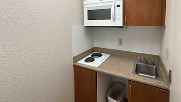 Une petite cuisine équipée d’un four à micro-ondes, d’une cuisinière, d’un évier et d’une poubelle.