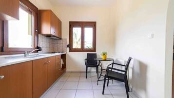 Een knusse keuken met houten kastjes, een betegelde achterwand, een raam en een kleine eethoek met twee stoelen en een tafel.