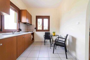 Eine kleine Küche mit Holdekor-Schränken, einer gefliesten Spritzschutzwand, einem Fenster und einer Essecke mit zwei Stühlen und einem Tisch.