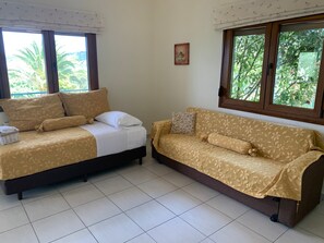 A room with a bed and a sofa, both with floral-patterned covers, a small basket with towels, and a picture on the wall. - Apartment 'Green Bay  Thassos' with Balcony, Wi-Fi and Air Conditioning (Κοίνυρα)
