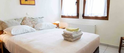 A bedroom with a bed, pillows, a bedside table with a lamp, a radiator, and a window with curtains.