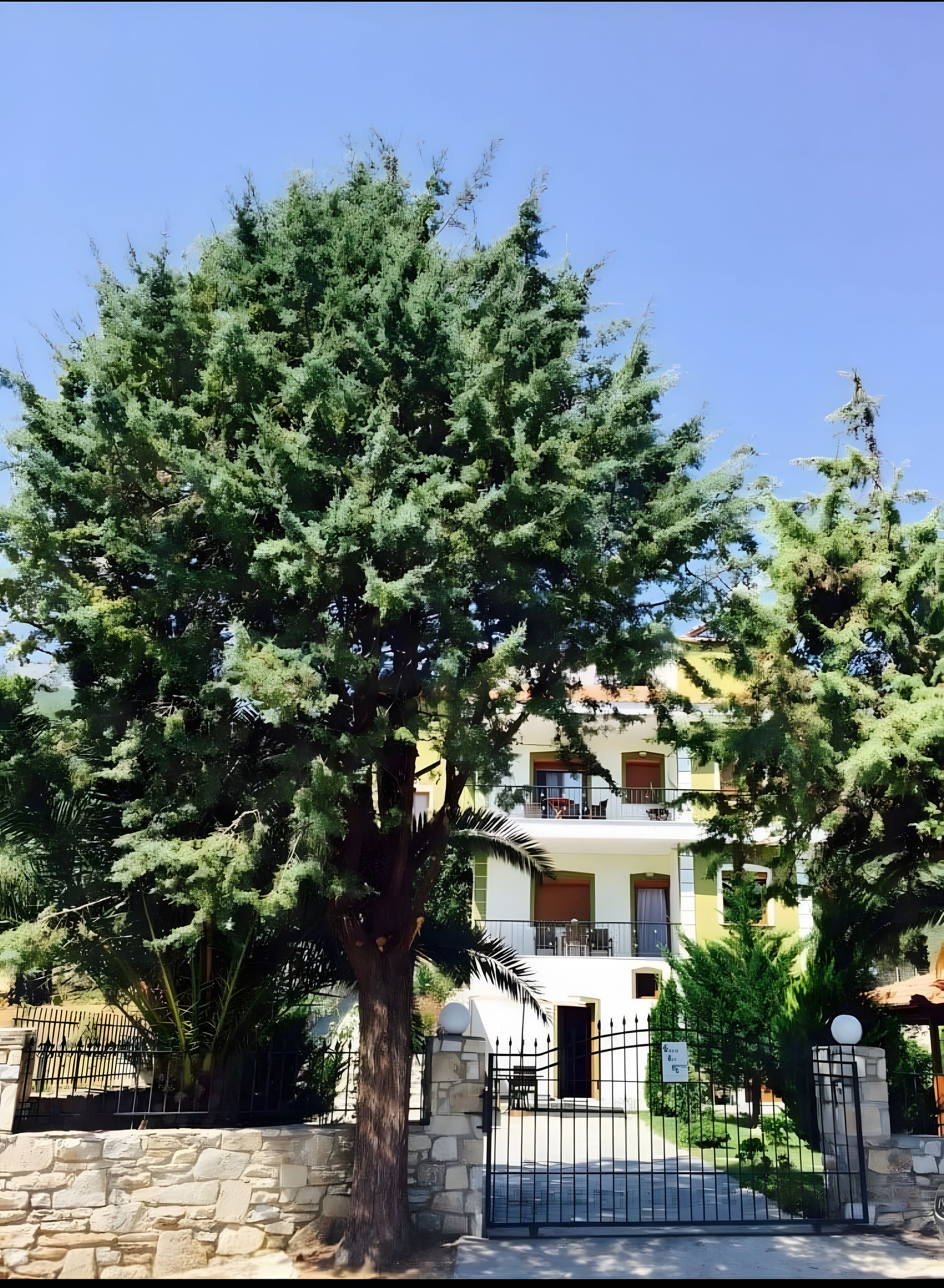 Un bâtiment à deux étages doté de balcons, entouré d’arbres et d’un mur de pierre.