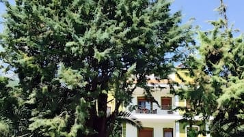 Un bâtiment à deux étages doté de balcons, entouré d’arbres et d’un mur de pierre.