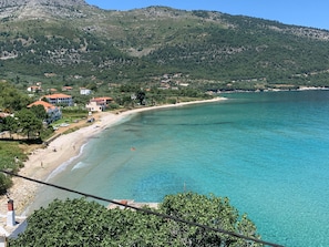 Paisagem costeira com praia, águas turquesa cristalinas e montanhas ao fundo.