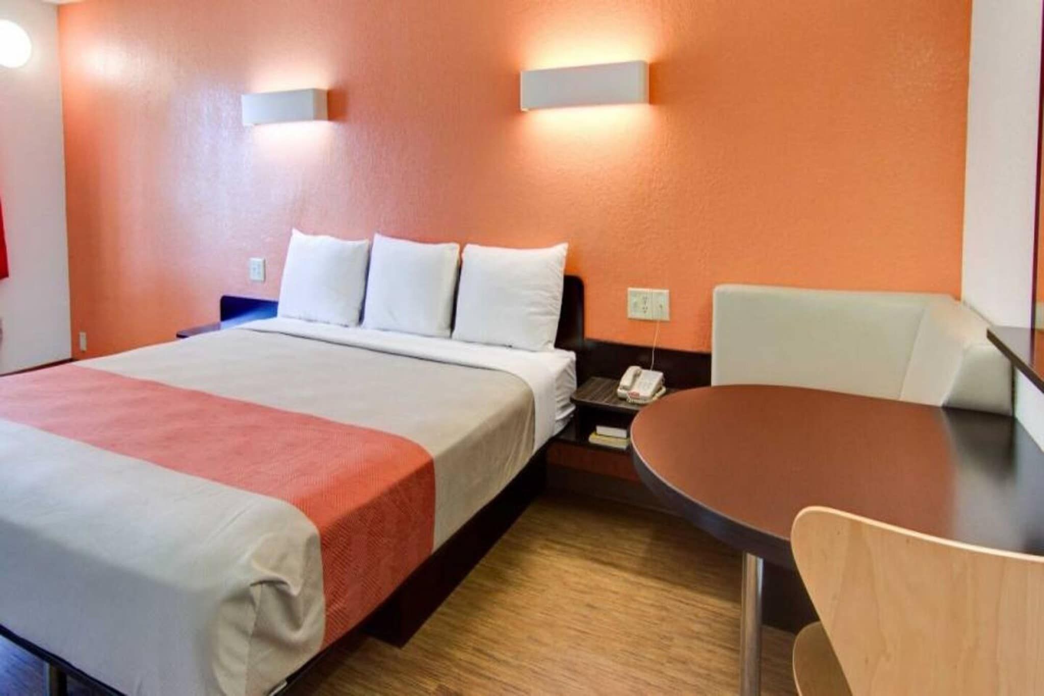 A hotel room with a bed, bedside table, chair, and a small table with a lamp.