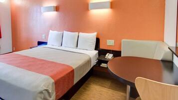 A hotel room with a bed, bedside table, chair, and a small table with a lamp.